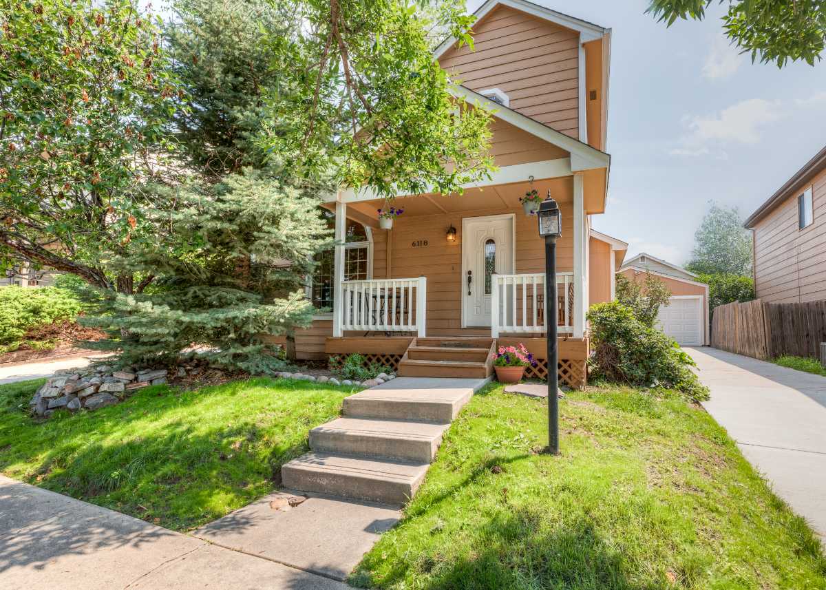 Charming Victorian-style cottage with white picket fence and covered front porch surrounded by mature trees in Colorado Springs | Top Tier Real Estate