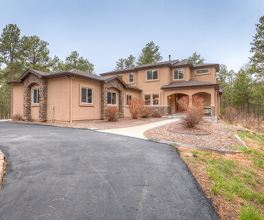 Spacious stucco and stone luxury home with curved driveway nestled among pine trees in Colorado Springs | Top Tier Real Estate